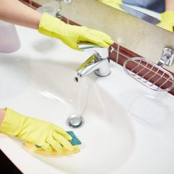 Gloved hands of hotel-maid during cleaning sink