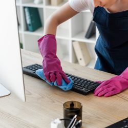 Cropped view of cleaner in rubber gloves cleaning computer keyboard in office
